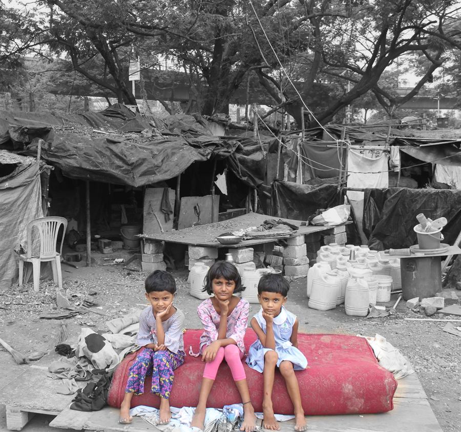 Three children sitting outside their homes in an informal settlement